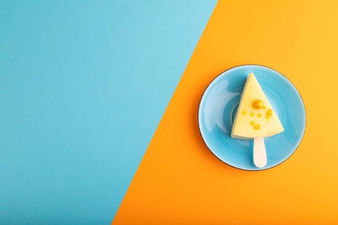 Yellow Cake pop with sprinkles on blue ceramic plate on blue and orange pastel paper background,