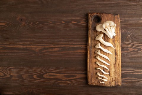 Raw Oyster mushroom, Pleurotus ostreatus on cutting board on brown wooden background. Top view,