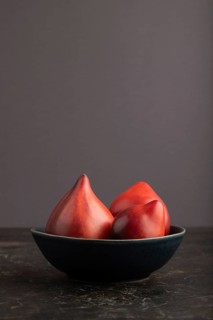 Red Heart shape tomatoes in blue bowl on black concrete background. Side view, copy space. healthy