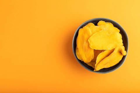 Dried Mango in blue ceramic bowl on orange pastel paper background. Top view, copy space, flat lay.