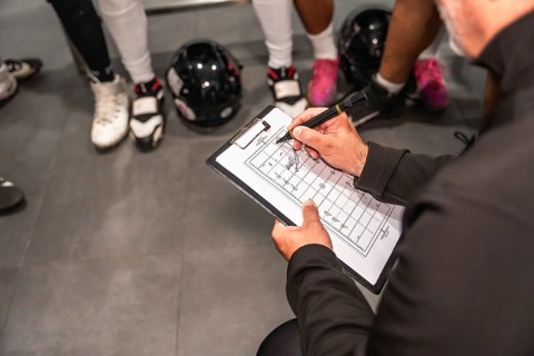 American football coach holding a clipboard, drawing strategies on a field diagram, instructing