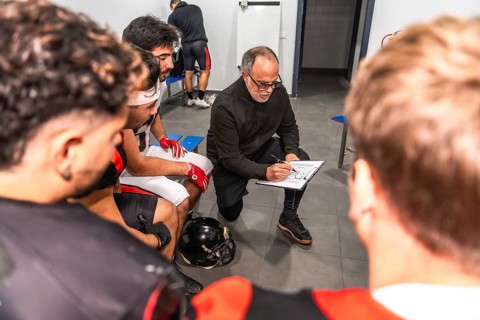 Football coach outlines game strategy on a clipboard while briefing his team in the locker room,