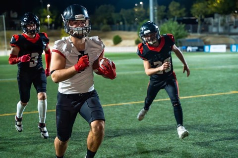 American football players, wearing protective helmets and pads, are running on a green turf field
