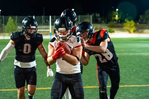 American football players in uniform and helmets engaging in a game on an illuminated sports field