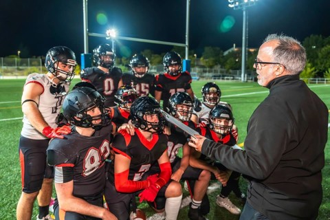 American football coach discussing strategy with his team of players in uniform and helmets during