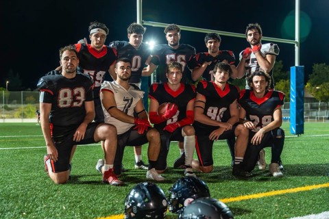 American football team in uniforms posing on illuminated turf at night, holding a ball and