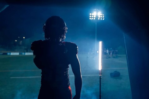 Football player standing in silhouette, ready to enter the stadium field at night, stadium lights
