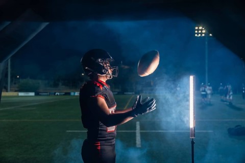 American football player in helmet and uniform lunging to catch a pass under stadium lights, smoke