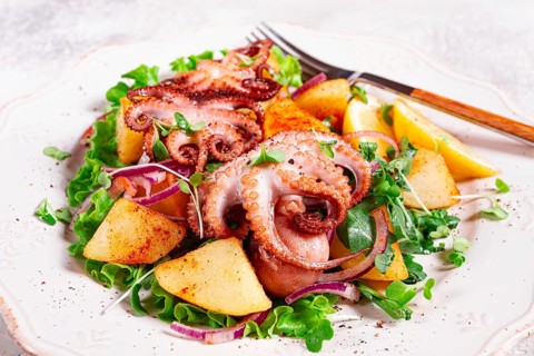 Grilled octopus with baked potatoes and fresh herbs, on a decorative light plate, homemade, no