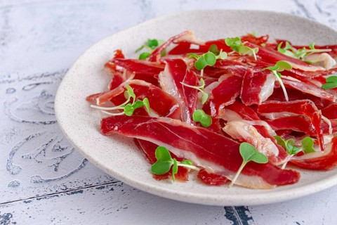 Ham of duck breast, dried duck fillet, with microgreens, plate, on a tiled table