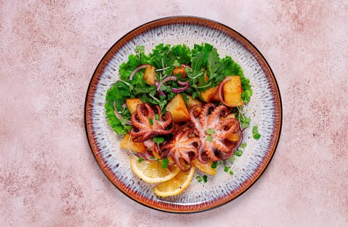 Grilled octopus with baked potatoes and fresh herbs, on a decorative plate, homemade