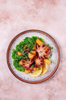 Grilled octopus with baked potatoes and fresh herbs, on a decorative plate, homemade
