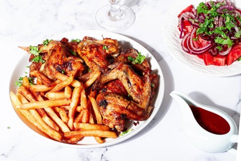 Delicious barbecue chicken wings, with French fries, salad and a refreshing drink, at a cozy table,