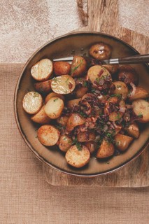 A bowl of perfectly roasted potatoes garnished with fresh herbs and caramelized onions sits on a