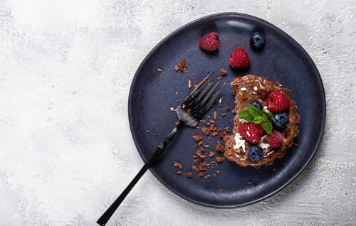 Half-eaten chocolate tartlet, on a plate, stuffed with cottage cheese and berries, breakfast,