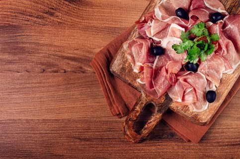 Sliced prosciutto, on a cutting board, with olives and herbs, snack, breakfast, no people