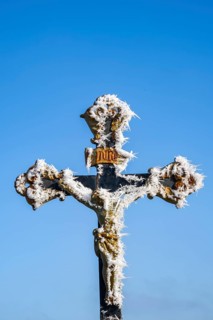 Crucifix with hoarfrost in front of blue sky at sunshine in winter, Bavaria, Germany