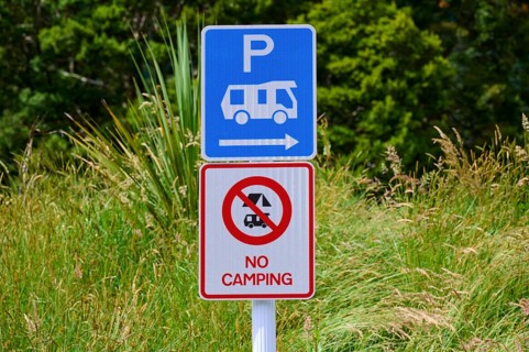 Ein Schild weist auf Parkmöglichkeiten für Wohnmobile hin und verbietet Camping, umgeben von Gras