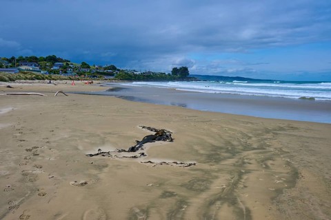 Weitläufiger Strand mit Meer, Wellen und entfernten Häusern unter einem leicht bewölkten Himmel,