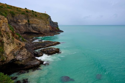 Dramatische Küstenlandschaft mit steilen Klippen Leuchturm und grünlich-blauem Meer unter einem