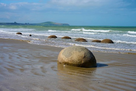 Große runde Felsen am Strand mit Wellen im Hintergrund und blauem Himmel, Moeraki Boulders,