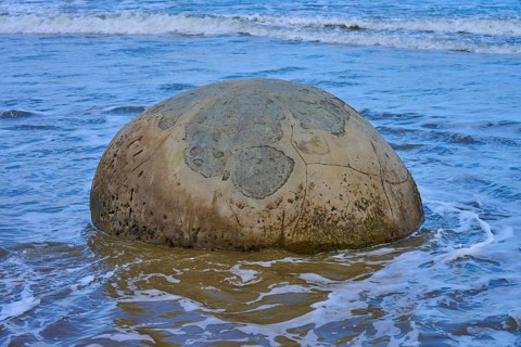 Ein großer runder Fels im seichten Wasser am Strand mit einem freien Blick auf das Meer, Moeraki