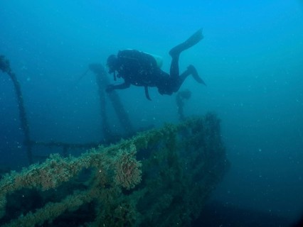 Diver floats above an overgrown wreck, exploring the depths of the sea. Dive site wreck of the Vis,