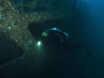 Diver examines a shipwreck with a lamp in the dark. Dive site wreck of the Vis, Pula, Croatia,