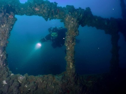 A diver explores the windows of a shipwreck with a lamp. Dive site wreck of the Baron Gautsch,