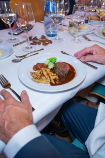 Steak with vegetables and pasta in an upscale dining environment with white tablecloth and wine