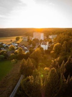 Aerial view of a village at sunset, surrounded by forests and fields, Tesla Model Y Juniper,