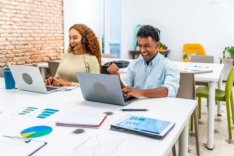 Diverse colleagues with headsets performing online customer service in an open plan office. A