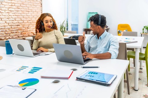 Diverse young professionals working in a modern office, wearing headsets, using laptops, and