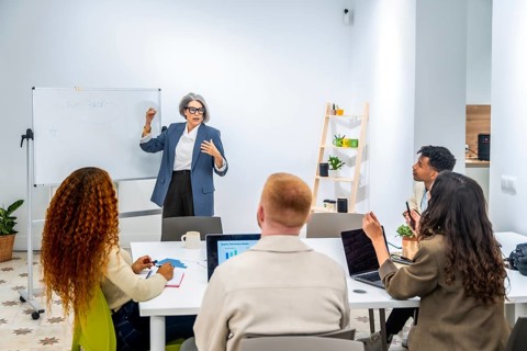 Senior grey haired business woman coaching and training a group of young, diverse professionals in