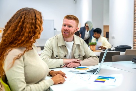 Diverse colleagues collaborate over charts and laptops in a modern coworking space, sharing ideas,