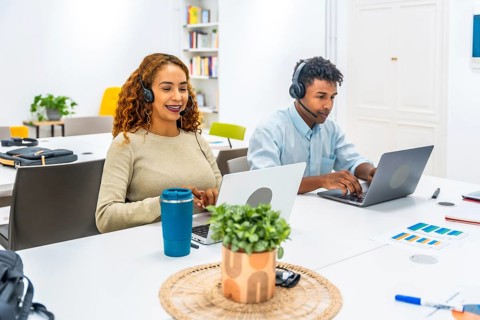 Customer service representatives wearing headsets and working on laptops, connecting with clients