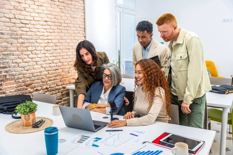 Diverse business professionals working together around a laptop, analyzing financial charts and
