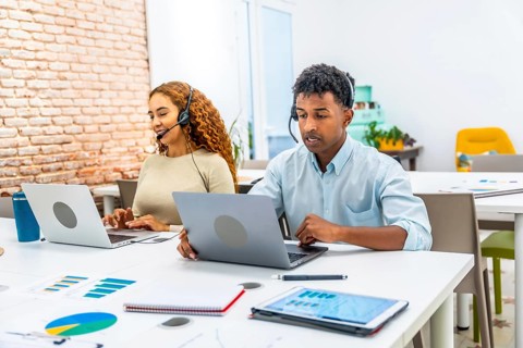 Multiracial customer service team wearing headsets and typing on laptops in a modern office,