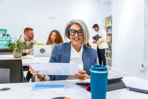 Happy mature businesswoman smiling at the camera, holding charts and graphs during a meeting with