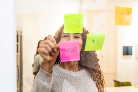 Happy woman collaborating on a project, writing ideas and tasks on colorful sticky notes on a clear