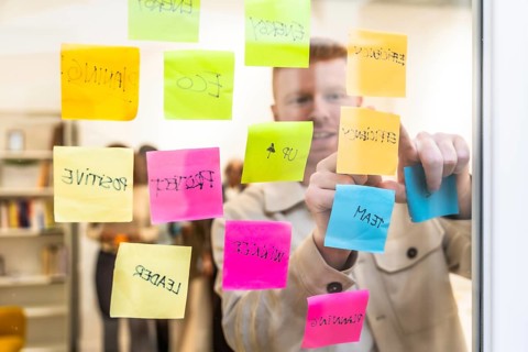 Man in a modern office space arranging colorful sticky notes with various concepts and keywords on