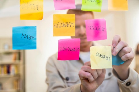 Red haired man organizing colorful sticky notes with handwritten words about planning, team, and