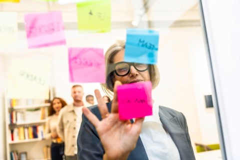 Mature businesswoman arranging colorful sticky notes on a glass board while leading a strategic
