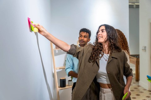 Diverse team collaborating, standing in a modern office, a smiling woman adding colorful sticky