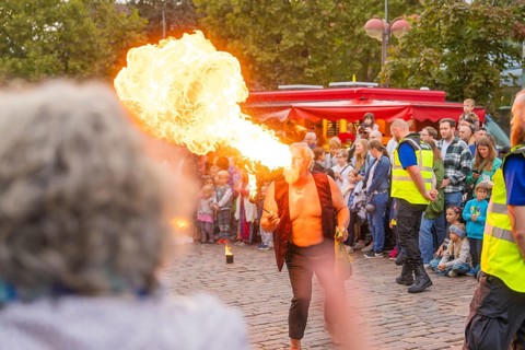A fire-eater performs an exciting show in front of a large audience on a cobbled street,