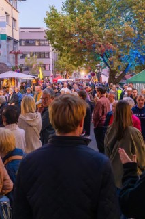 A crowd strolls through a street at dusk, lined with trees and lights, Fire Night, Sindelfingen,