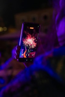 Person holding a mobile phone showing a photo of colourful fireworks at night, Fire Night,