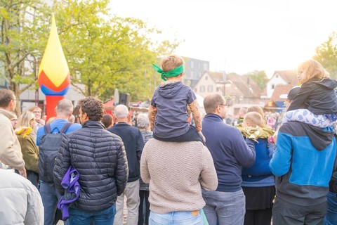 People gather under trees in sunny weather with colourful decorations in the background, Fire