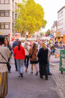 Many people stroll through a busy street at a city festival, trees and colourful clothes