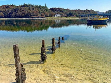 Shoreline landscape with clear water and a yellow boat, calm atmosphere, Silver Sands of Morar,